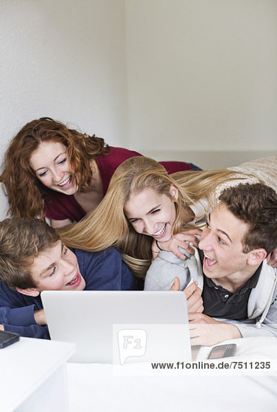 Happy young friends with laptop in bed