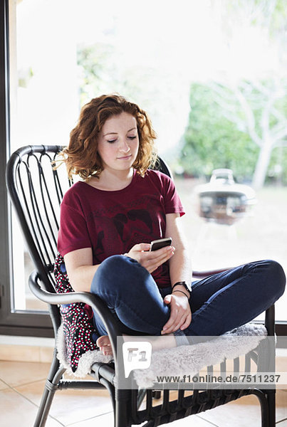 Junge Mädchen SMS beim Entspannen auf dem Sessel zu Hause