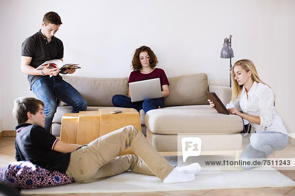 Junge Jungen und Mädchen mit Magazin  Laptop und digitalem Tablett im Wohnzimmer