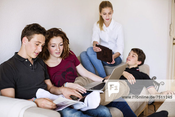 Teenager-Freunde mit Laptop und digitalem Tisch diskutieren im Wohnzimmer