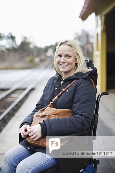 Porträt einer glücklichen behinderten Frau im Rollstuhl auf dem Bahnsteig des Bahnhofs