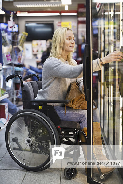 Behinderte Frau im Rollstuhl im Kühlbereich des Supermarktes