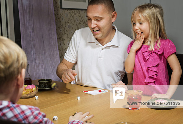 Vater mit Kindern beim Würfelspiel am Tisch