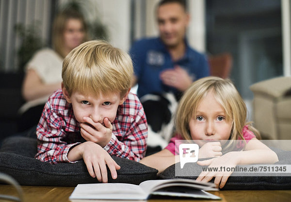 Portrait of little siblings with book lying on front and parents in background