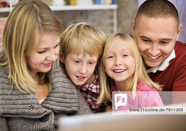Porträt eines glücklichen Mädchens mit Familie  das den Laptop zu Hause benutzt.