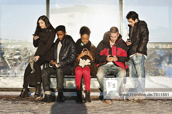 Group of multi ethnic friends using mobile phones on bench