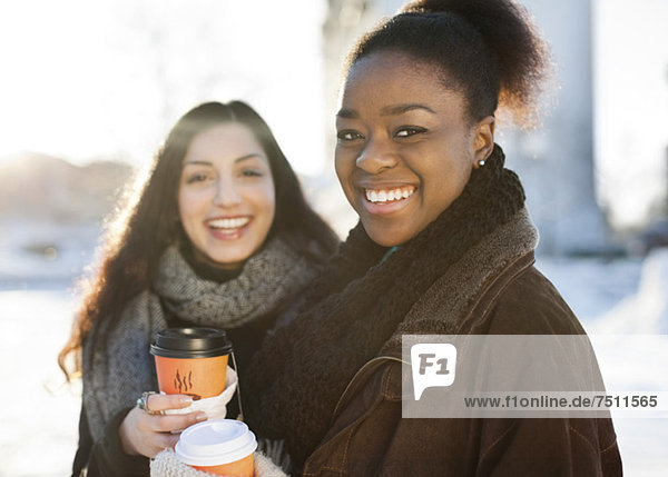 Portrait von glücklichen Freundinnen in warmer Kleidung mit Einwegbechern