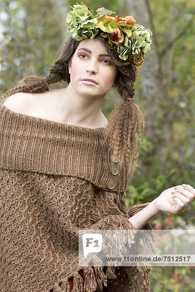 Young woman wearing a brown poncho with a flowal wreath in her hair  outdoors