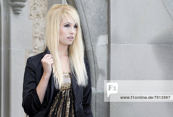 Young woman with long blonde hair wearing a black jacket posing in a stone arch