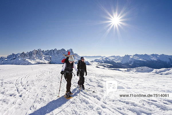Snowshoe hiker and a cross-country skier ascending Uribrutto Mountain  looking towards the Palla Group and Passo Rolle pass  Dolomites  Trentino  Italy  Europe