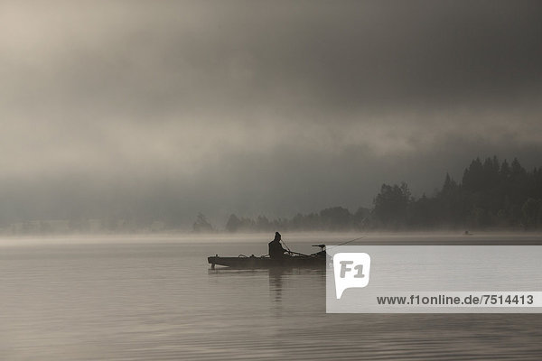 Fisherman early in the morning with fog in the morning light on Weissensee lake  Carinthia  Austria  Europe