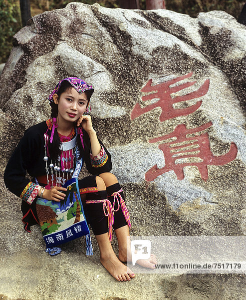 Junge Miao Frau in ethnischer Tracht  Felsen mit chinesischer Inschrift  Hainan  China  Asien