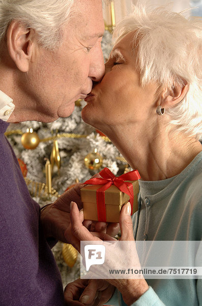 Älteres Pärchen beschenkt und küsst sich vor dem Weihnachtsbaum