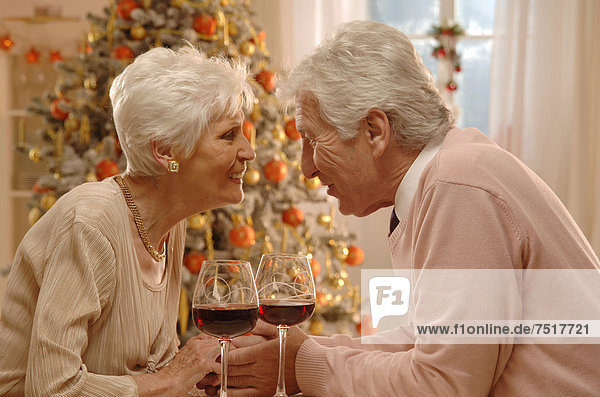 Mature couple with red wine glasses sitting in front of a Christmas tree