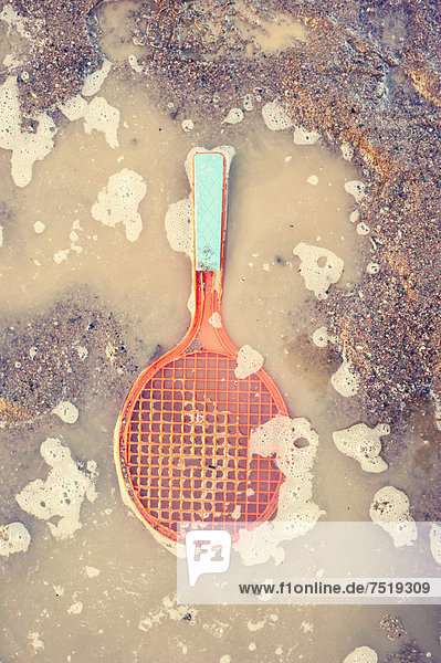 Plastikspielzeug  ein Tennisschläger liegt in einer schmutzigen Pfütze