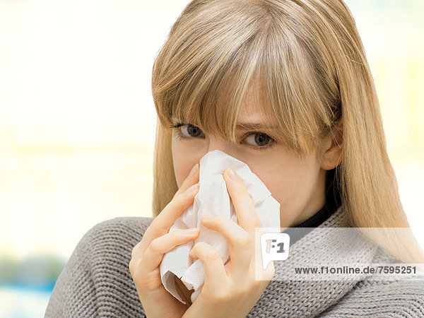 Junge Frau mit Taschentuch  putzt sich die Nase  krank  Allergie