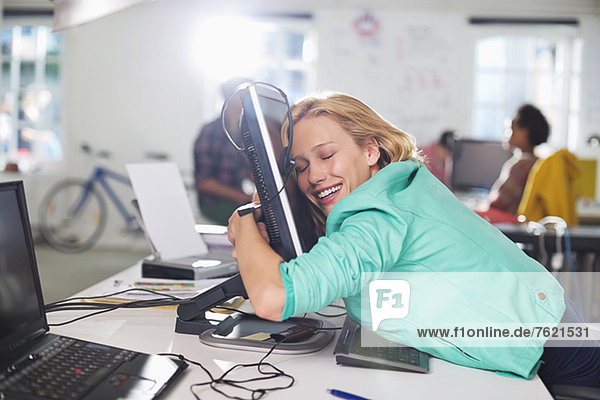 Geschäftsfrau umarmt Computer am Schreibtisch
