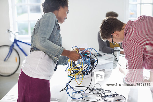 Business people untangling cords in office