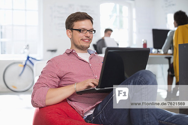Businessman using laptop in bean bag chair in office