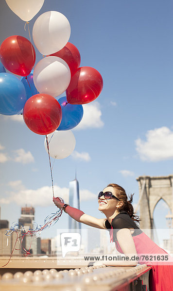 Woman holding bunch of balloons on urban bridge