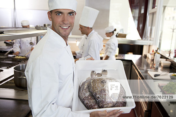 Chef carrying tub of fresh fish in restaurant kitchen