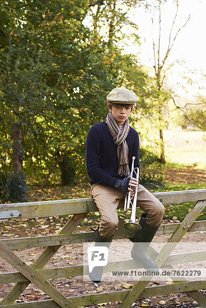 Teenager-Junge hält Trompete auf Holzzaun