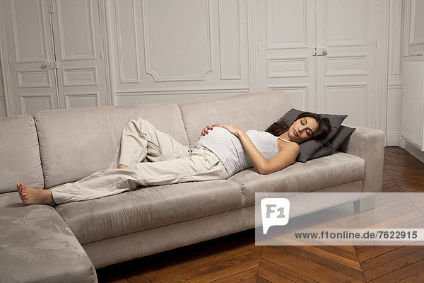 Schwangere Frau hält Bauch auf Sofa
