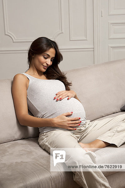 Pregnant woman holding belly on sofa
