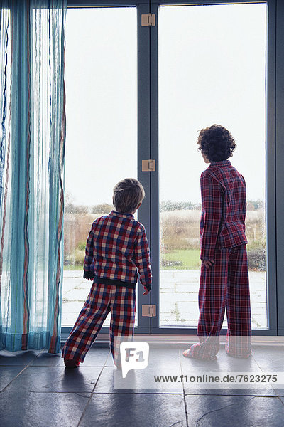 Boys in pajamas looking out window
