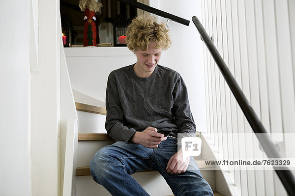 Teenager-Junge mit Handy auf der Treppe
