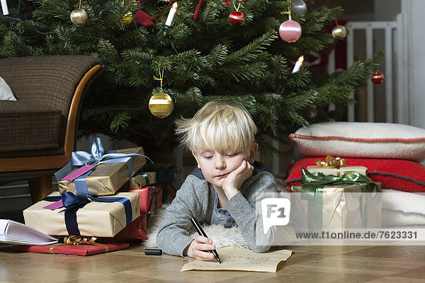 Junge schreibt unter dem Weihnachtsbaum