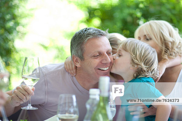 Junge küsst Vater bei Tisch im Freien