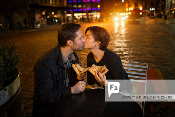 Küssendes Paar beim Pizza essen im Freien