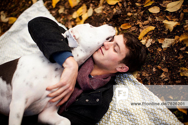 Mann und Hund umarmen sich auf Picknickdecke