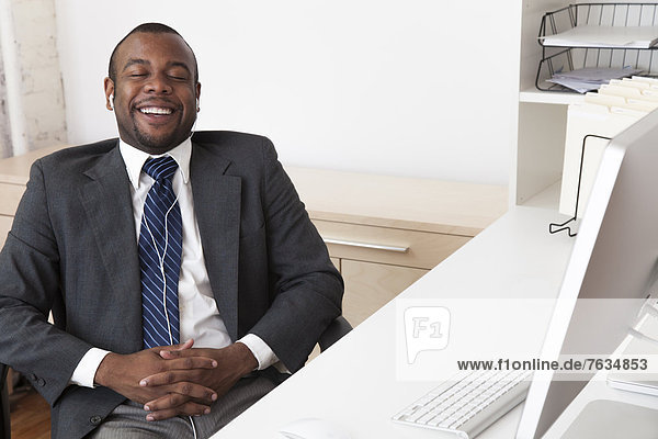 Black businessman listening to music at desk in office
