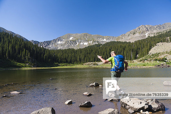 Caucasian hiker climbing on rocks in lake