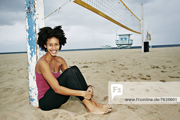 Mixed race woman sitting by volleyball net on beach