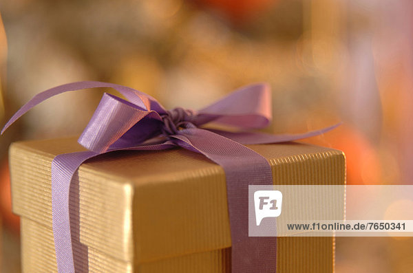 Goldene Geschenkebox mit lila Schleife vor Weihnachtsbaum