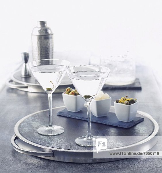 Zwei Martinis auf einem Silbertablett  Oliven  Kapern  Silberzwiebeln und Cocktailshaker