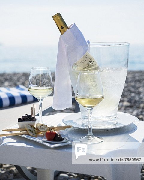 Gedeckter Tisch am Strand mit Vorspeisen  Weissweingläsern und Weinflasche im Kühler