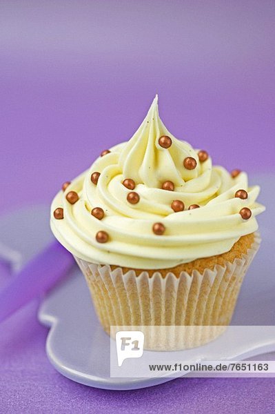 Cupcake mit Vanillecreme und Goldperlen im Papierförmchen