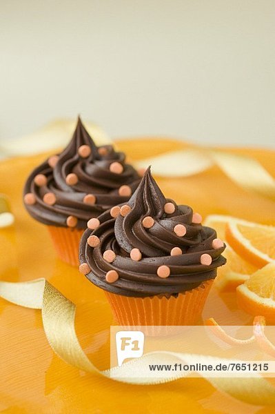 Zwei Schokoladencupcakes mit Zuckerkonfetti und Orangen
