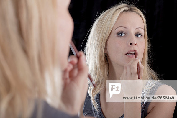 Young blonde woman applying lipstick in front of a mirror  make-up