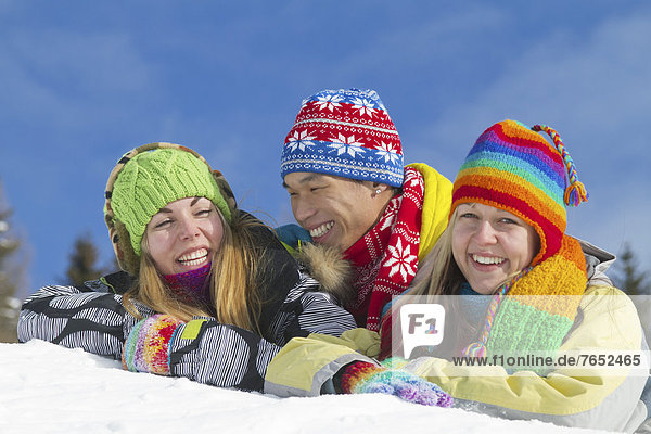 Young Asian man and two young European women smiling while lying on a mound of snow and wearing colourful winter clothing  Villach  Carinthia  Austria  Europe
