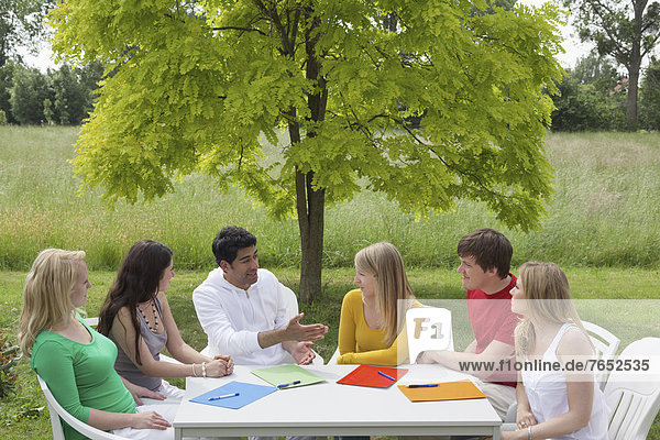 Six young people having a discussion around a round table in a garden  Hagen  Lower Saxony  Germany  Europe