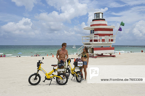 Couple riding electric bicycles  Watchtower  The Jetty  Miami Rescue Tower  South Beach  Miami  Florida  USA
