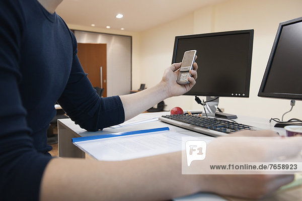 Man working at desk in office  holding cell phone  mid section
