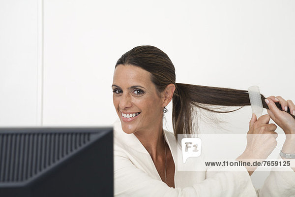 Reife Geschäftsfrau beim Haareputzen am Schreibtisch