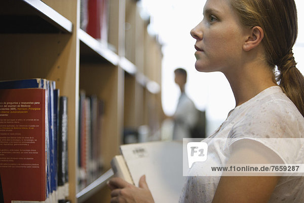 Young woman looking at books in library