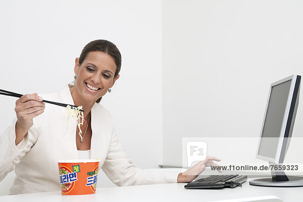 Reife Geschäftsfrau beim Essen von Instant-Nudeln am Schreibtisch
